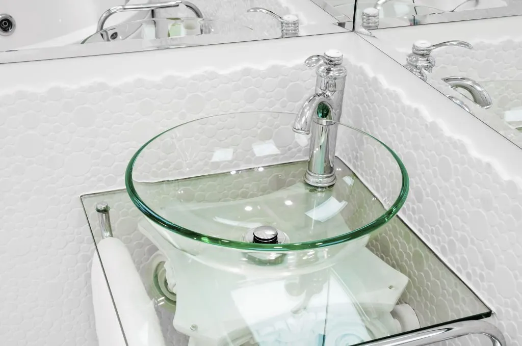 Glass washbasin on glass table and corner mirror in bathroom
